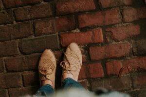 Image of two feet in tan shoes standing outside on a brick sidewalk.